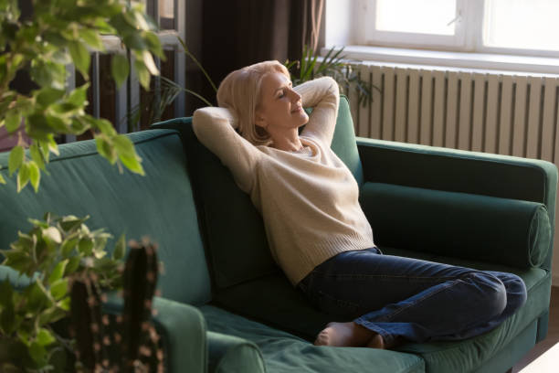 Middle age woman resting on couch daydreaming at home