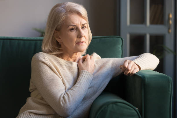 mujer madura deprimida perdida en pensamientos sentados en el sofá - menopausia fotos fotografías e imágenes de stock