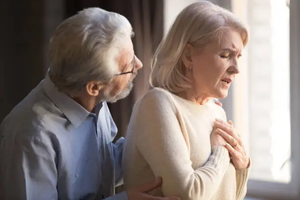 Photo of Elderly wife holding hand on chest worried husband supporting her