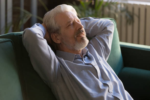 istock Grey haired senior man sitting leaning on couch recovers strength 1158702235