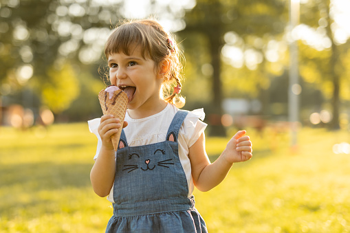 Beautiful baby girl eating ice cream on a sunny summer day. Child with sunglasses holding ice cream in her hand