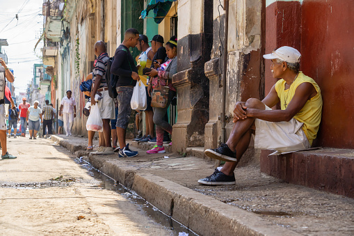 Havana, Cuba - May 16, 2019: People sitting on the sidewalk in the Old Havana City during a vibrant and bright sunny day.