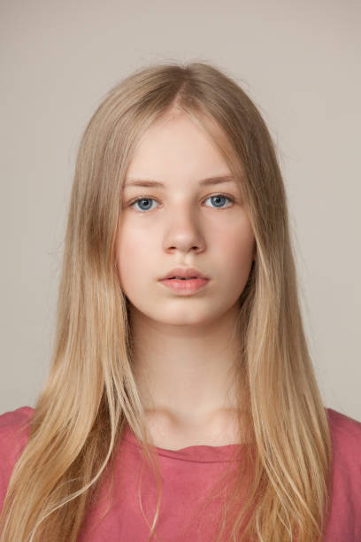 studioporträt eines blonden teenager-mädchens in einem rosa t-shirt auf beigefarbenem hintergrund - teenage girls blue eyes adolescence teenager stock-fotos und bilder