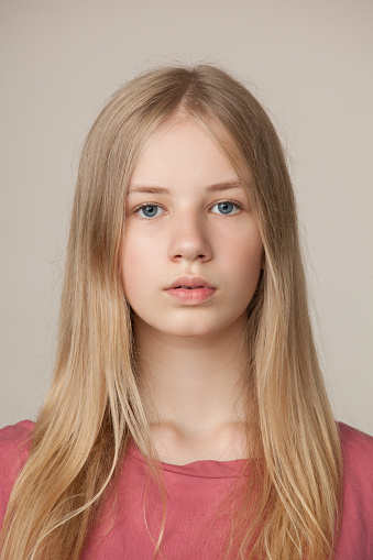 Studio portrait of a blonde teen girl in a pink t-shirt on a beige background
