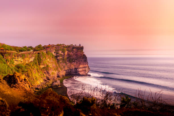 인도네시아 발리의 험준한 풍화 절벽 가장자리에 있는 울루와투 사원의 일몰과 인도양의 해안, 그리고 분홍색 황혼하늘 이면 - bali temple landscape seascape 뉴스 사진 이미지