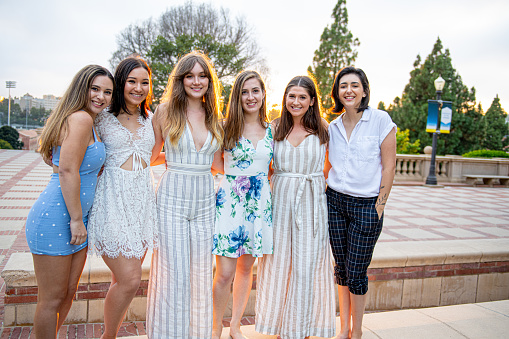 Six close girlfriends pose  for a group graduation photo on their college campus.