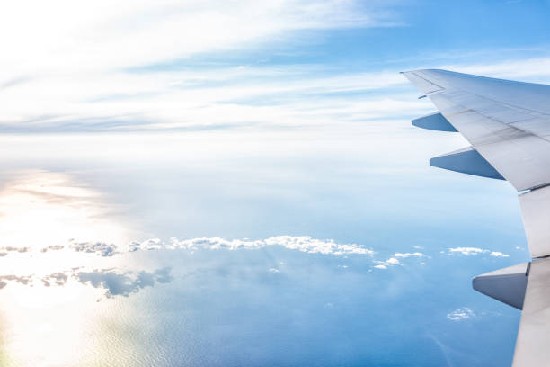 istock White airplane in blue sky with view from window high angle during sunny day with plane wing and sun setting above horizon with light path 1158718690