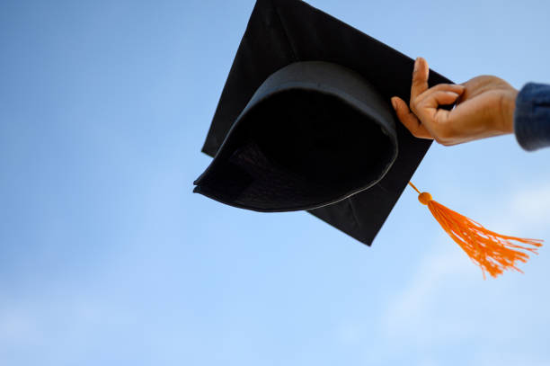 istock Graduates hold a black hat with a yellow tassel attached to the sky. 1158719186