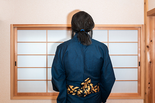 Traditional japanese house with sliding door window with back of man in kimono costume standing with obi sash belt