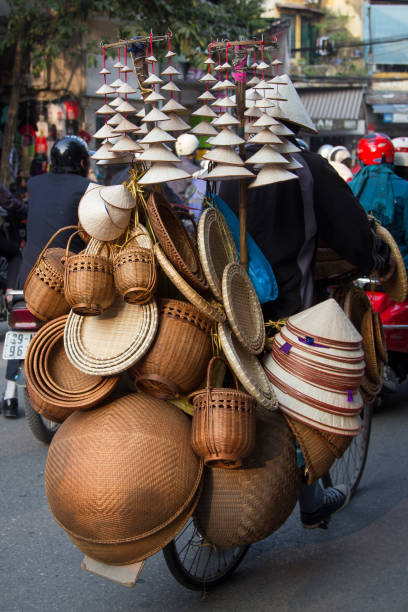 Ho Chi Minh City, Vietnam – August 28, 2019: A traditional Vietnamese street vendor is seen carrying fruits in baskets balanced on a bamboo pole while walking along the sidewalk in central Ho Chi Minh City. The scene reflects everyday local life and street trade culture in Vietnam.
