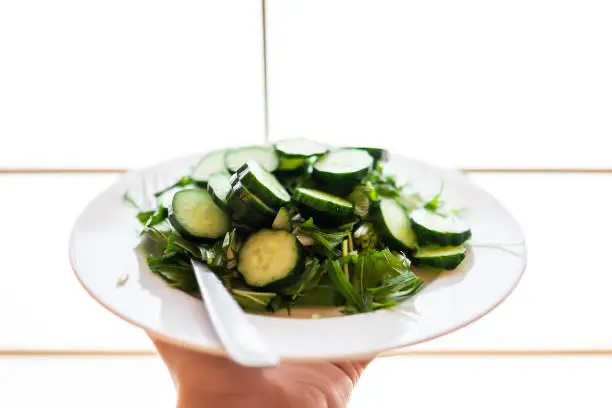 Home or restaurant with hand holding green salad dish closeup with Japanese cucumbers and mizuna greens with background of shoji