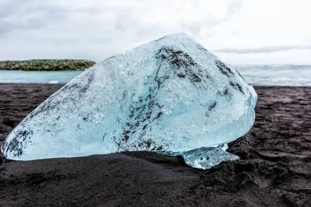 Closeup of cold one blue glacier iceberg in Jokulsaron lagoon lake diamond beach in Iceland with black sand on shore