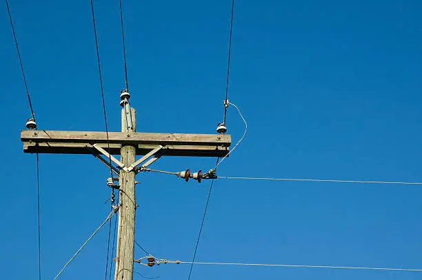 An electical pole with wires and insulators against a clear blue sky with write space.