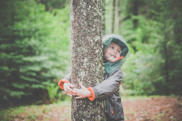 istock Little Redhead Boy Embracing a Tree and Wearing Mosquito Netting Hat 1158741167
