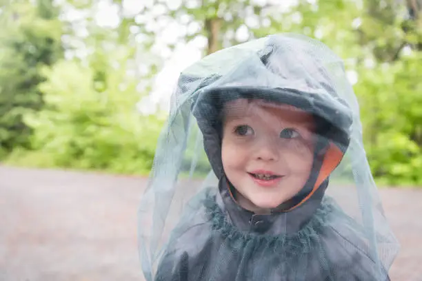 Photo of Little Redhead Boy Playing Outside on Campground and Wearing Mosquito Netting Hat