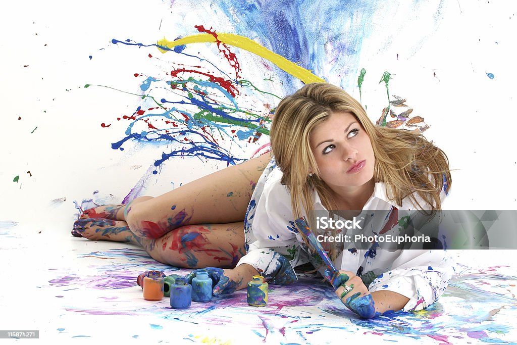 Beautiful young woman painting in a white room Beautiful young woman laying in paint covered studio.  Paint splattered on walls, floor, model.  Shot in studio over "white".  :) Paint Stock Photo