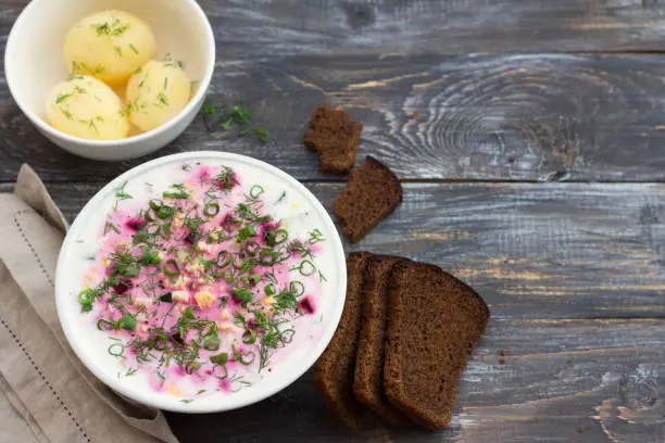 Delicious summer soup, beetroot soup (svekolnik, holodnik) on kefir, with cucumber, boiled eggs and greens. traditional Lithuanian, Russian, Ukrainian, Belorussian or Polish cuisine. healthy homemade food. on a wooden table. top view