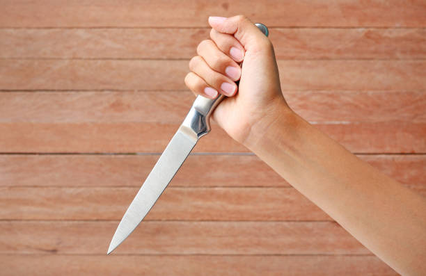 istock Hand holding a knife ready to strike down against plank wood 1158744318