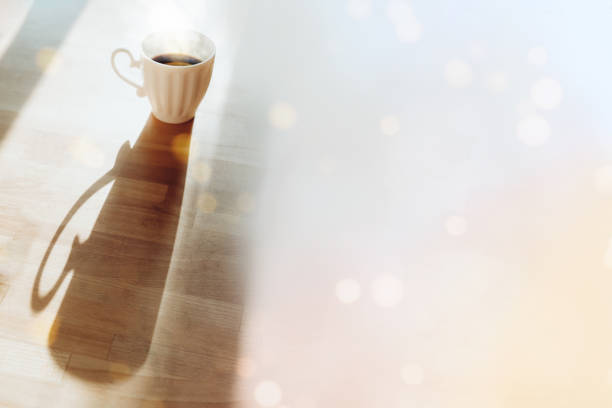White cup with espresso standing on wooden table with long shadow side view. Breakfast tea with bokeh lights image. Good morning concept. Mug with hot drink, coffee beverage horizontal background