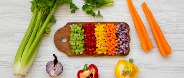istock Chopped fresh vegetables (carrot, celery, onion, colored peppers) arranged on a cutting board on a white wooden surface, top view. Overhead, from above, flat lay. 1158749016