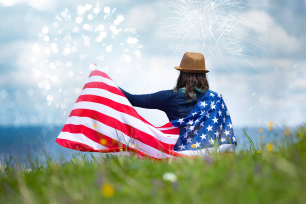 Young happy patriot girl holding the american flag under the 4th of July fireworks.