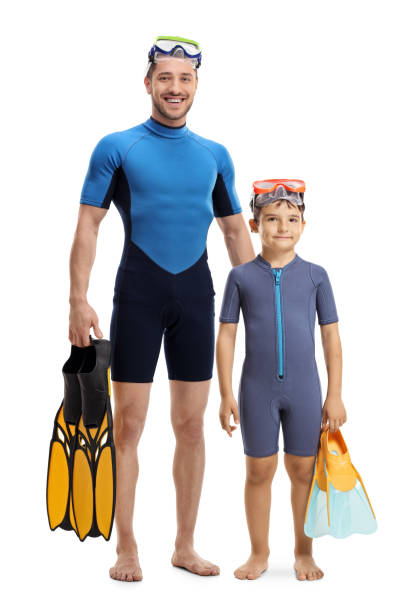 Child and man in wetsuits standing and holding diving flippers