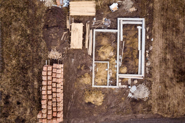 istock Concrete foundation for basement of future house, stacks of bricks and building timber logs for construction on sunny summer day, aerial view. 1158754276