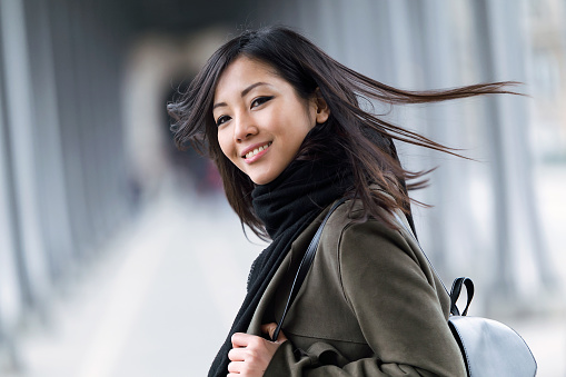 Portrait of pretty asian young woman smiling and looking at camera in the street.