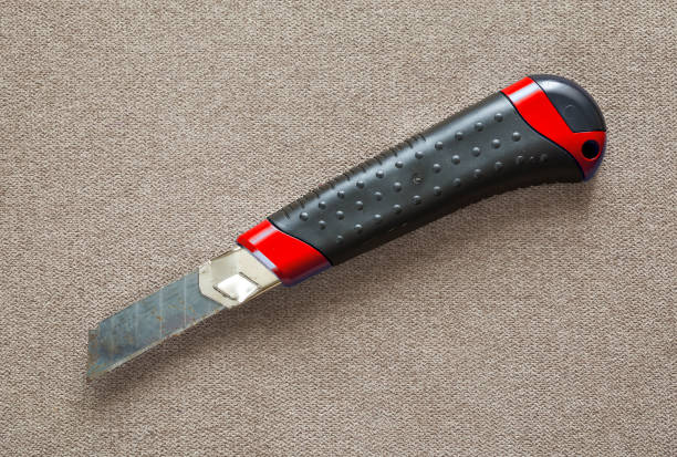 Close-up of isolated stationery retractable metallic knife with sharp blade on light cloth copy space background.