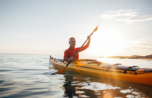 Senior man paddling kayak on a sunset sea.