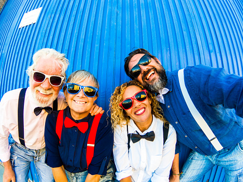 Two caucasian couples have fun and smile at the camera for a selfie. Behind them a blue striped wall. Concept of cheerfulness and positivity for two generations of family