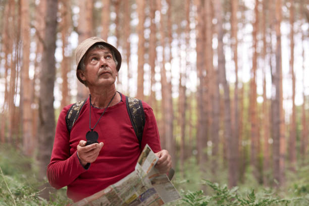 Close up shot of eldery man hiking and looking up at sky, using map and compass for direction for trip in forest, traveling around world, having adventure in wood, enjoying his active vacation. de cerca de tiro de anciano hombre de senderismo y mirando hacia el cielo, utilizando el mapa y la brújula para la dirección para el viaje en el bosque, viajar por el mundo, tener aventura en la madera, disfrutar de sus vacaciones activas.