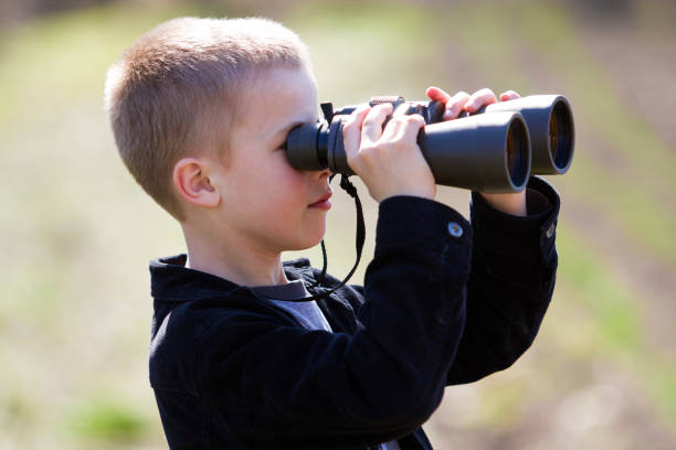 istock Portrait in profile of little handsome cute blond boy looking thoughtfully through binoculars in distance on blurred background. Children dreams, fantasies and imaginations concept. 1158762396