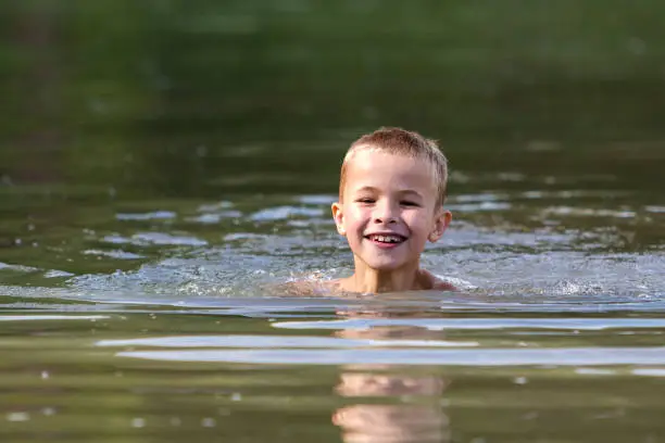 Photo of Young smiling child boy swimming in muddy water on sunny summer day. Active lifestyle and safety.