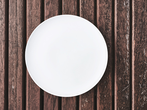 White plate on wooden table, space for text, food concept