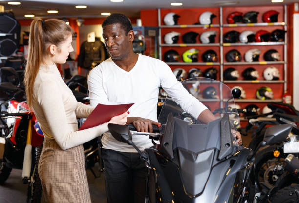 vendedor femenino amable y sonriente que se comunica con el cliente masculino en el salón de motos moderno - extremal fotografías e imágenes de stock