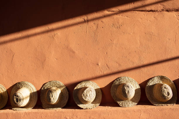 istock Straw beach hats standing on terracotta  clay wall.  Bright sunlight and hard shadows. 1158764931