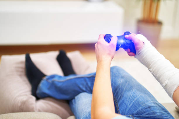 Man with broken arm in plaster cast holding controller and playing in videogame in front of TV. Game addiction concept. stock photo