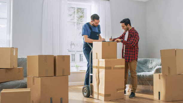 happy new homeowner begrüßt professional mover mit hand truck voller kartons, erhält seine waren und schilder auf derablage. - mover stock-fotos und bilder