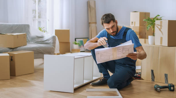 el trabajador exitoso del ensamblaje de muebles lee las instrucciones para ensamblar estante. manitas profesionales haciendo trabajo de montaje bien, ayudando a las personas que se mudan a new house. - furniture fotografías e imágenes de stock