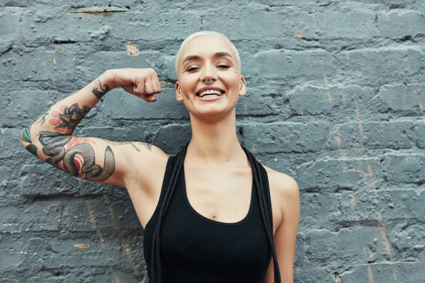 Check my progress Cropped portrait of an attractive young woman flexing her biceps while working out against a gray background tattoo arm stock pictures, royalty-free photos & images
