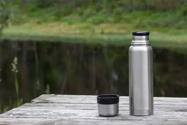 Thermos and cup on wooden table in forest