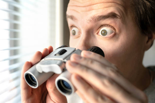 hombre sorprendido con binoculares. un tipo curioso con ojos grandes. vecino entrometido acechando o husmeando secretos, chismes y rumores. cara tonta y graciosa. conmocionado por noticias increíbles. - entrometido fotografías e imágenes de stock