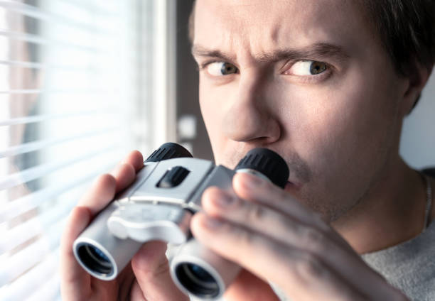 istock Suspicious, skeptic and confused man with binoculars. Conspiracy theory, paranoia, skepticism or suspicion concept. Curious or paranoid person looking out the window. 1158779111
