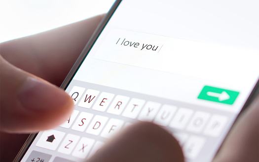 Sending I love you text message with mobile phone. Online dating, texting or catfishing concept. Romance fraud, scam or deceit with smartphone. Man writing comment. Fake profile. Internet safety.