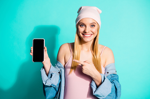 Portrait of her she nice attractive lovely charming cute cheerful girl wearing streetstyle clothing pointing at device gadget isolated on bright vivid shine blue green turquoise background