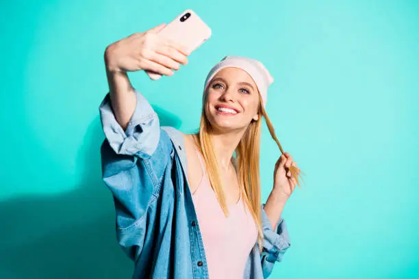 Portrait of her she nice attractive, lovely fascinating charming cute cheerful girl wearing streetstyle clothing taking making selfie isolated on bright vivid shine blue green turquoise background