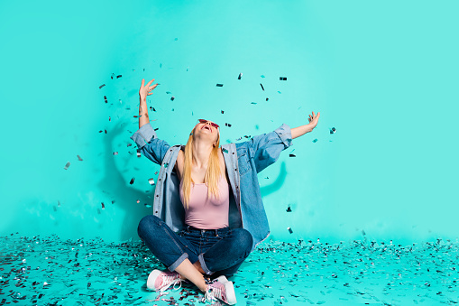 Portrait of her she nice, attractive cheerful cheery glad excited girl sitting on floor rest relax flying decorative elements isolated on bright vivid shine blue green turquoise background