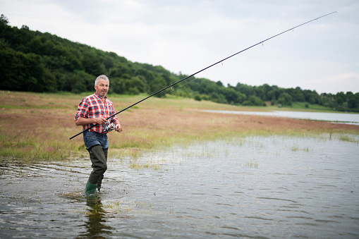 Adult man in water holding fishing rod, looking at camera and smiling.
