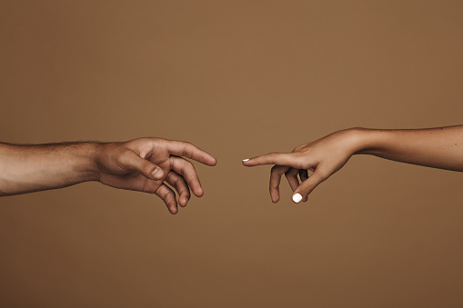 Close up of man and woman hand about to touch with index finger. Couple in love reaching to one another in front of brown background.